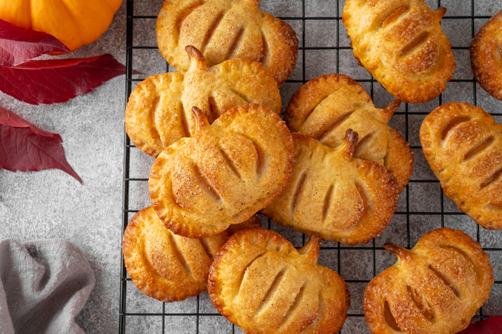 Pumpkin mini pies or hand pies with glass of coffee on a stone background. Traditional autumn dessert for Halloween and Thanksgiving. Copy space