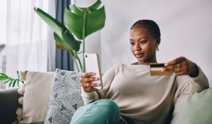 Shot of a young woman using her card and phone to shop online at home