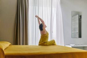 Mature woman stretching sitting on bed in hotel room